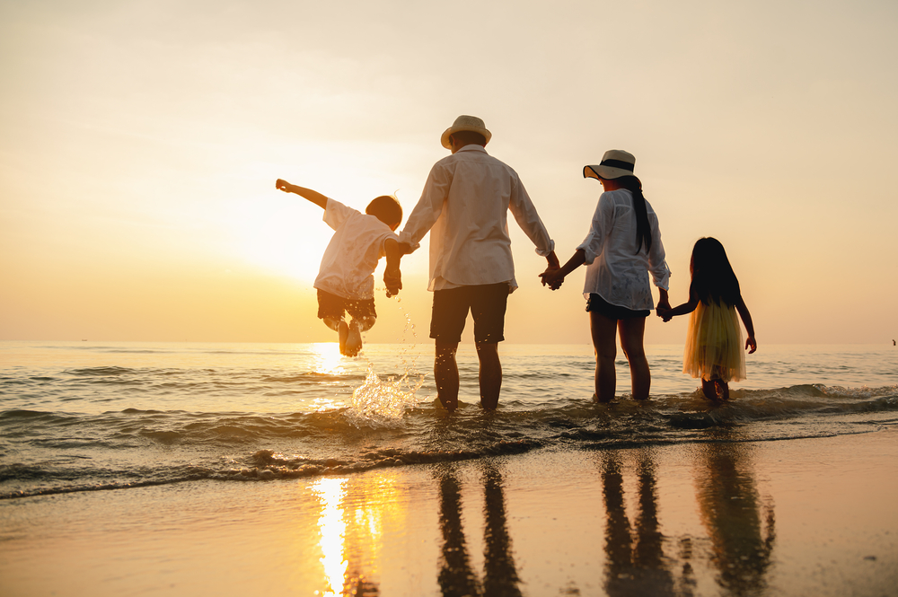 Feliz familia saltando juntos en la playa de vacaciones con la puesta de sol de fondo